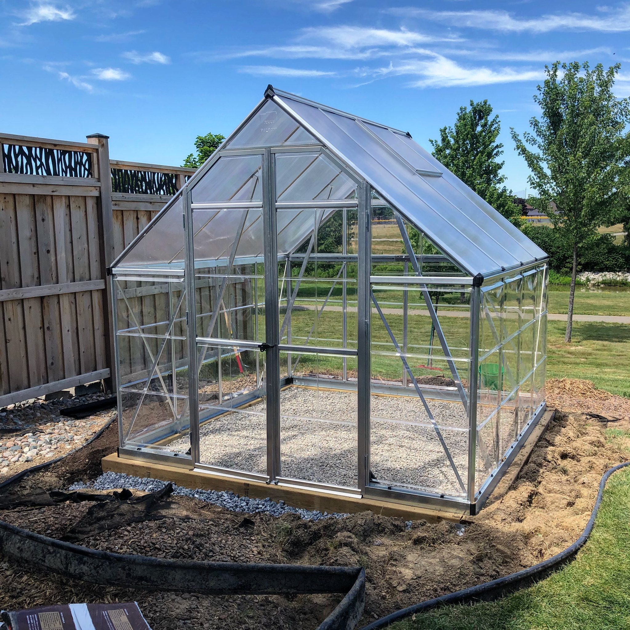 A pressure-treated wood foundation supporting a polycarbonate backyard greenhouse kit